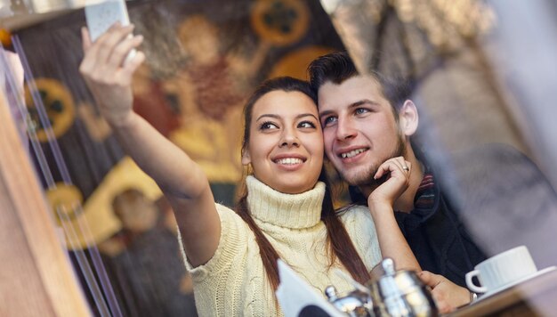 Trendy koppel dat een selfie maakt met een telefoon, in een coffeeshop