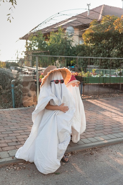 Foto trendy laken geesten kostuums op kleine kinderen staan op een buitenwijk straat gelukkige halloween vakantie