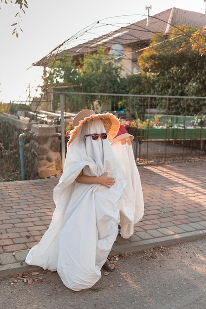 Foto trendy laken geesten kostuums op kleine kinderen staan op een voorstad straat gelukkige halloween vakantie