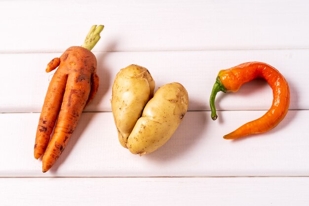 Trendy lelijke gebogen wortel, peper en aardappel op witte houten achtergrond.