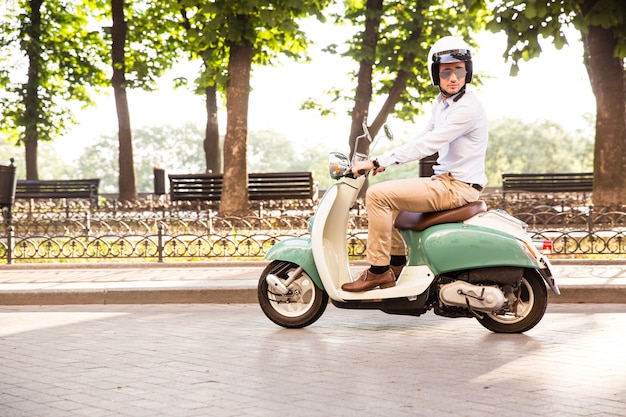 Uomo alla moda che guida uno scooter nel casco