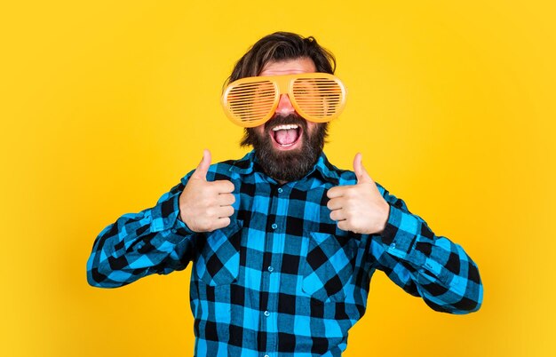 Trendy man in een grappige feestbril grappige en vrolijke man draagt een geruit overhemd, gewoon plezier maken, blije brutale feestganger, volwassen bebaarde hipster in een goed humeur, modeconcept, duim omhoog