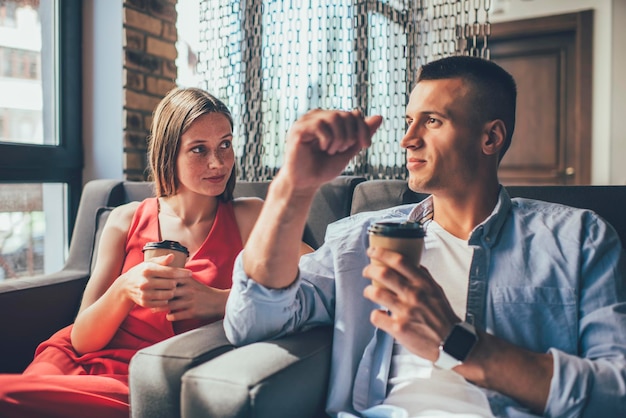 Trendy man and woman having coffee chilling in armchairs