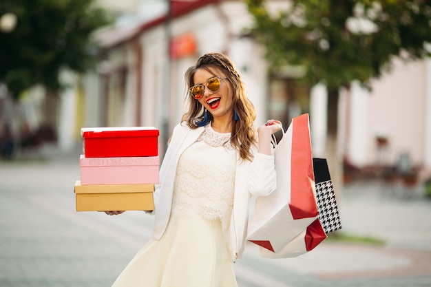 Trendy meisje in zonnebril met schoendoosjes en boodschappentassen in t