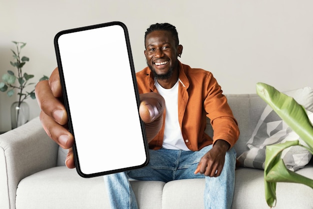 Trendy mobile phone Happy black man holding smartphone with white empty screen showing device to camera mock up