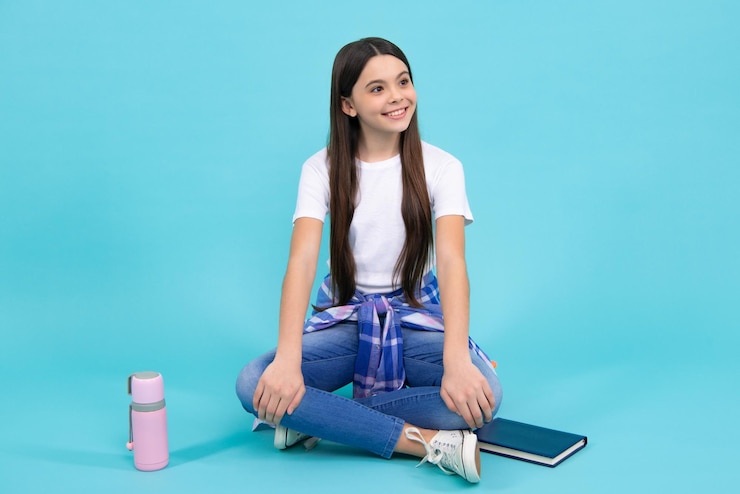Foto trendy mooie tiener model poseren op blauwe studio achtergrond kind meisje in tshirt en jeans studio opname tiener mode gelukkig tiener positieve en lachende emoties van tiener meisje