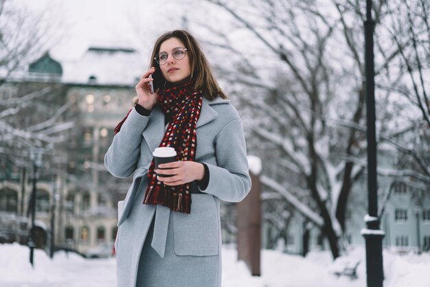 Trendy mooie volwassen vrouw in winteroutfit met afhaalmaaltijden en praten op mobiel