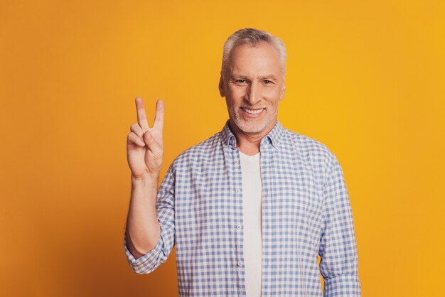 Trendy old man showing v-sign isolated yellow background