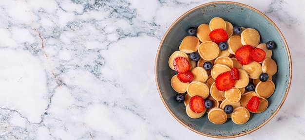 Trendy ontbijt met mini pannenkoeken, bosbessen en aardbeien, bovenaanzicht.