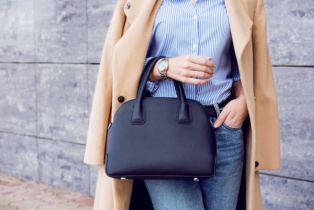 Foto trendy outfit vrouw in stijlvolle beige jas en spijkerbroek met zwarte big bag