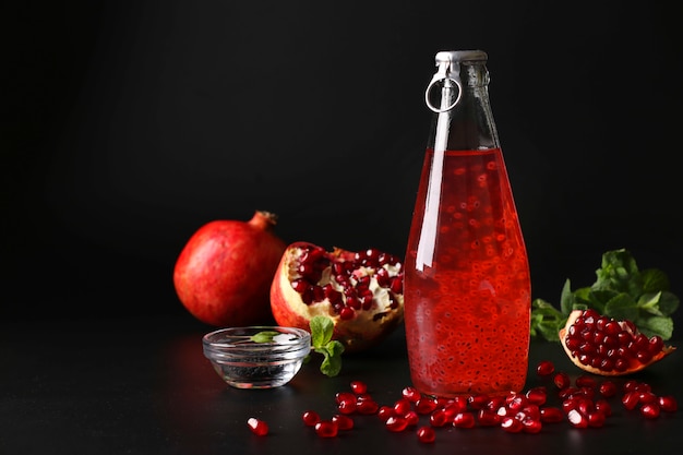 Trendy pomegranate drink with basil seeds in bottle on black background, Closeup