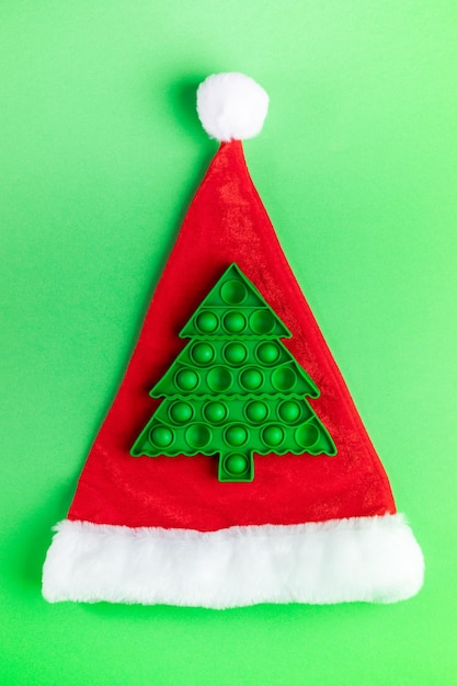 Trendy popular child anti stress pop it toy in form of green Xmas tree on red Santa's hat on green