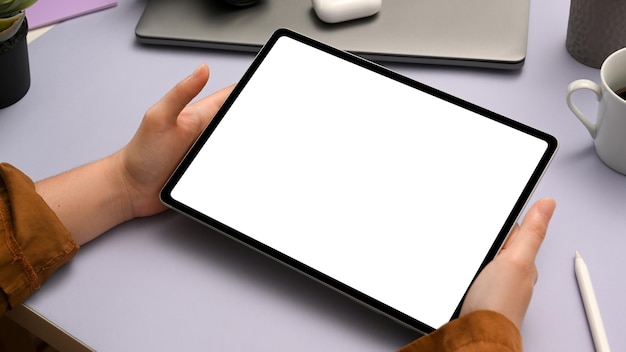 女性の手のクローズアップでデジタルタブレット空白の空の画面のモックアップとトレンディな紫色のオフィスデスク