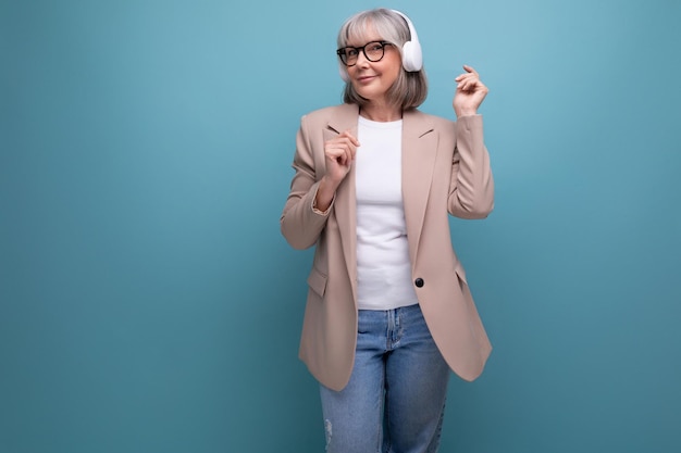 Trendy s woman in a stylish jacket listens to music in big headphones on a bright background with