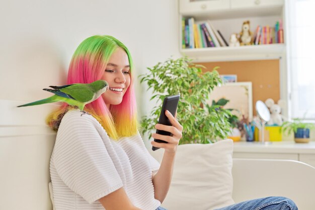 Trendy tienermeisje met smartphone en quaker papegaai op haar schouder