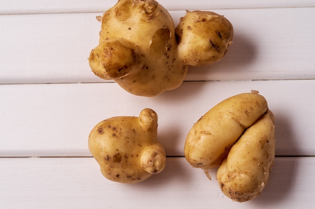 Trendy ugly curved potatoes on white wooden background.