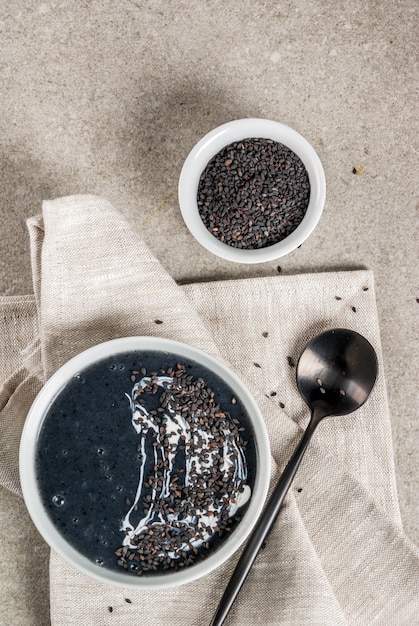 Ricette alla moda vegane, zuppa di sesamo nero con semi di sesamo e latte di cocco, tavolo in pietra grigia, vista dall'alto di copyspace