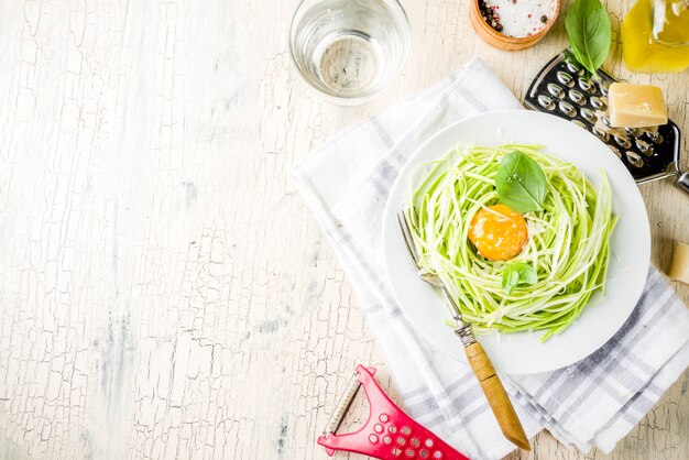 Trendy veganistische recepten, kaas courgette spaghetti pasta met eierdooier met parmezaanse kaas, olijfolie en basilicum, licht betonnen oppervlak