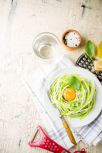 Trendy veganistische recepten, kaas courgette spaghetti pasta met eierdooier met parmezaanse kaas, olijfolie en basilicum, licht betonnen oppervlak