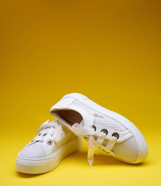 Foto sneaker bianche alla moda in pelle perforata con spesse suole di gomma su uno sfondo giallo gradiente