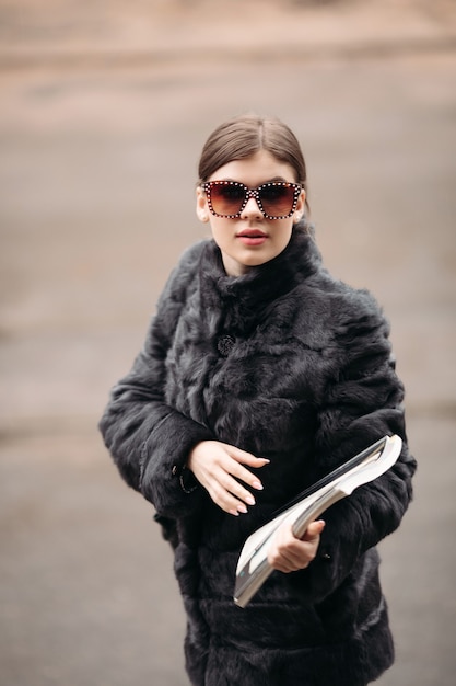 Trendy woman in fur coat and sunglasses posing on street