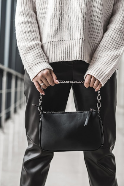 Trendy young girl in a warm cozy sweater shows off a stylish black leather bag