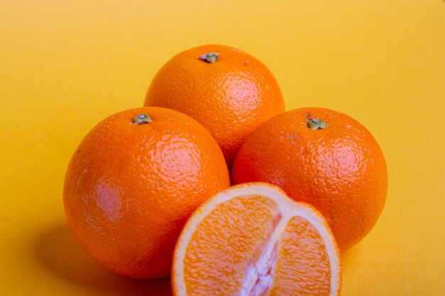 Photo tres naranjas frescas sobre fondo amarillo con una naranja partida por la mitad delante, fruta fresca