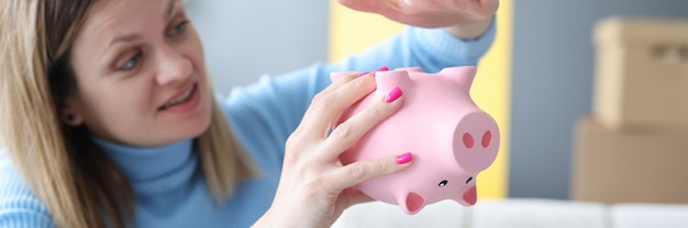 Treurige vrouw die haar hand op roze spaarvarken close-up slaat