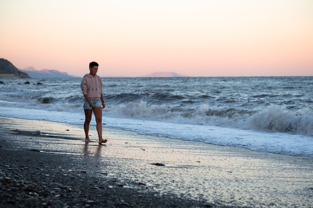 Treurige vrouw loopt langs het strand met dramatische koude golven