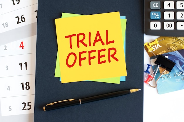 Trial offer, text on yellow paper square shape. Notepad, calculator, credit cards, pen, stationery on the desktop. Business, financial and education concept. Selective focus.