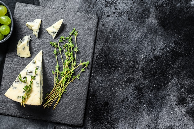 Triangle of blue cheese with grapes on cutting board. Black background. Top view. Copy space