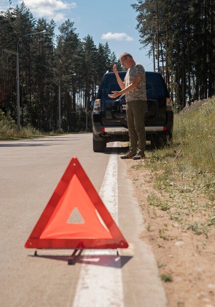 Triangle caution sign on road after car breakdown and driver talking on phone waiting for emergency ...