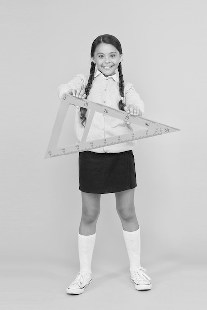 A triangle has three sides and three angles Adorable happy schoolchild holding triangle on yellow background Cute girl smiling with geometric triangle for geometry lesson Lesson in triangle