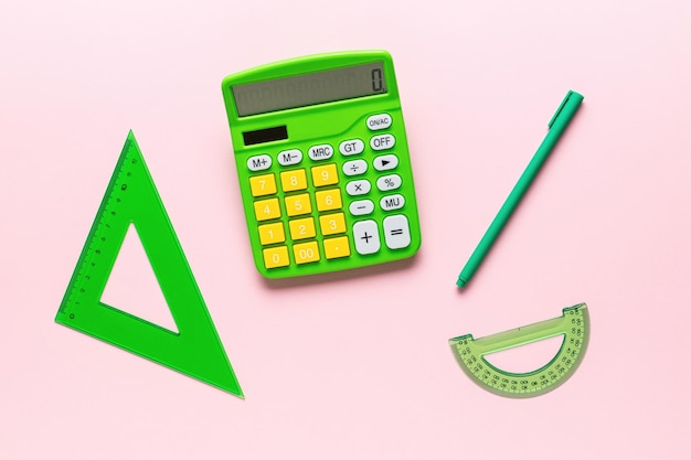 Triangle protractor pen and calculator are green on a pink background A set of school supplies Flat lay