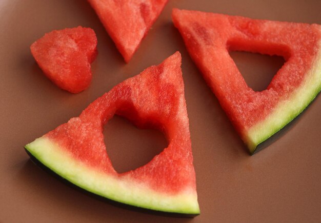 Triangular pieces of watermelon with a heart carved from watermelon pulp in a brown cup