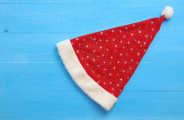 Triangular Santa Claus cap with stars on blue wooden background