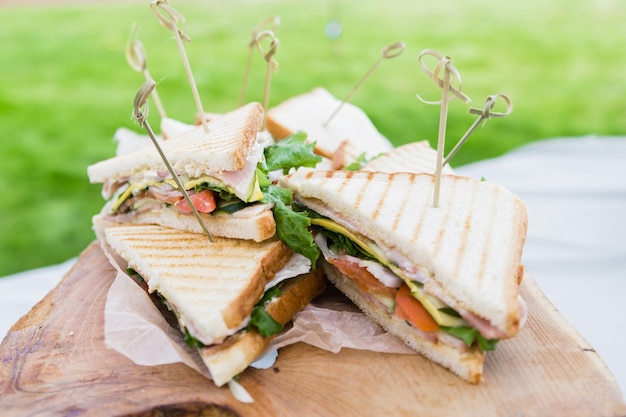 Triangular shaped sandwich with ham vegetables and mayonnaise on a wooden platter Menu for an outdoor event in summer Horizontal photo