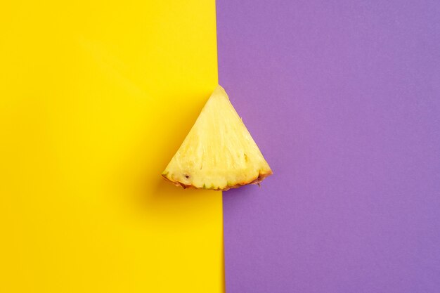 파인애플의 삼각형 조각 노란색과 보라색 배경에 놓여
