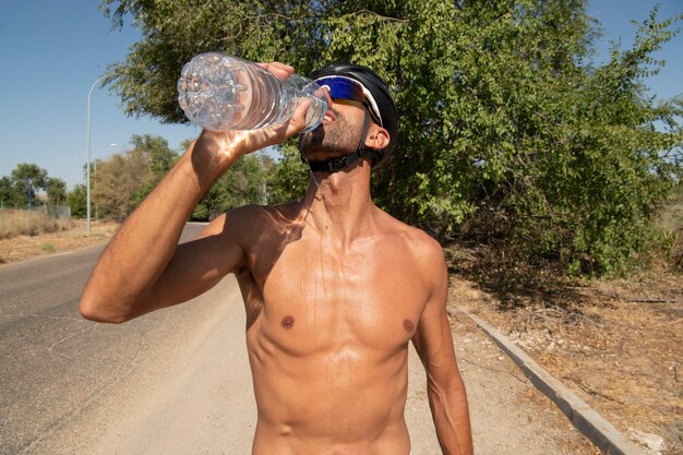 サングラスをかけ、シャツを脱いでボトルから水を飲むトライアスリート。