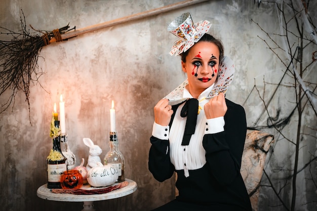 Trick or treat. portrait of young woman with spooky makeup\
wearing queen of hearts costume with card collar looking at camera\
through spider web while visiting night halloween party
