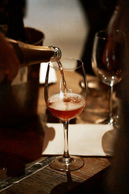 A trickle of pink champagne fills the glass on the wooden table. 