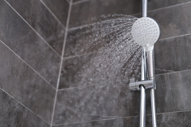 Trickles of water flowing from shower head in bathroom closeup