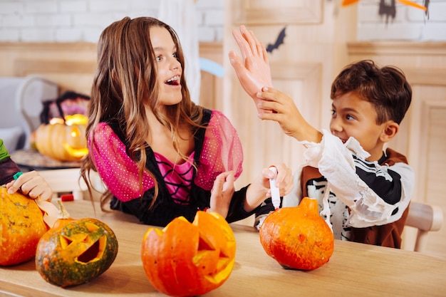 Tricks with sister. Cute dark-eyed boy wearing skeleton Halloween costume plating tricks with older sister