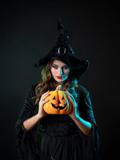 Tricky beautiful witch in a pointed hat holding a pumpkin with a laughing face