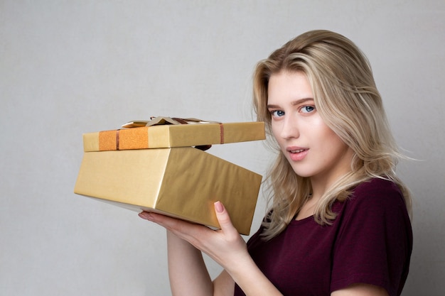 Tricky blonde woman looking to the gift box over a grey background