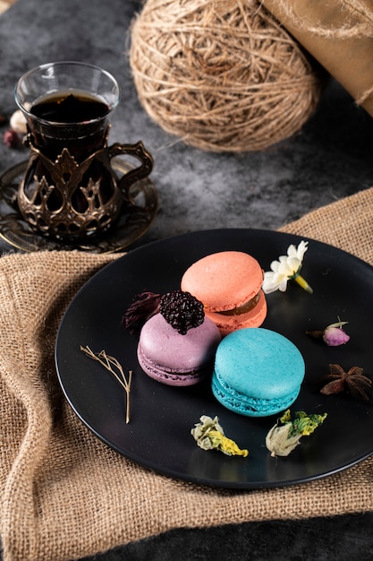 Tricolor French macarons on a black saucer and a glass of tea. top view