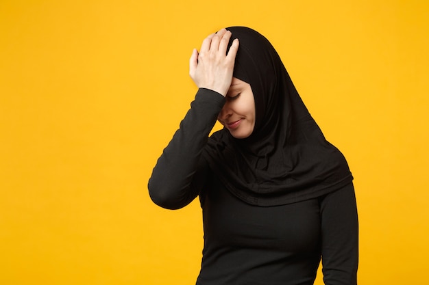 Triest boos huilende verwarde jonge Arabische moslimvrouw in hijab zwarte kleding poseren geïsoleerd op gele muur portret. Mensen religieuze islam levensstijl concept.