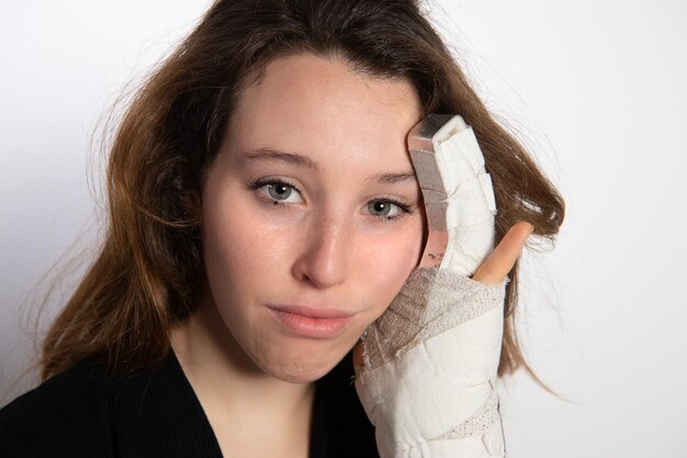 Triest brunette vrouw leunend gebroken hand op haar gezicht Vrouw met witte pols bandage en metalen fixatie van gebroken vinger Stress breuk letsel in de hand Pijn ongevallen en gezondheidszorg conceptxDxA