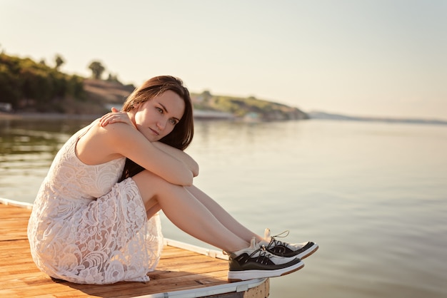 Triest eenzame jonge vrouw zitten knuffelen haar knieën op de pier met droevige ogen, eenzaamheid, scheiding, apathie, depressie