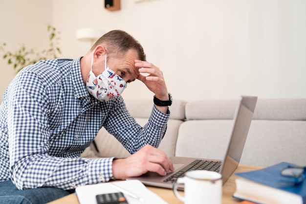 Triest freelancer met online zakelijke bijeenkomst en zittend op de bank Bezorgde zakenman met medisch beschermend gezichtsmasker chatten op laptop terwijl hij thuis op de computer werkt Online conferentie